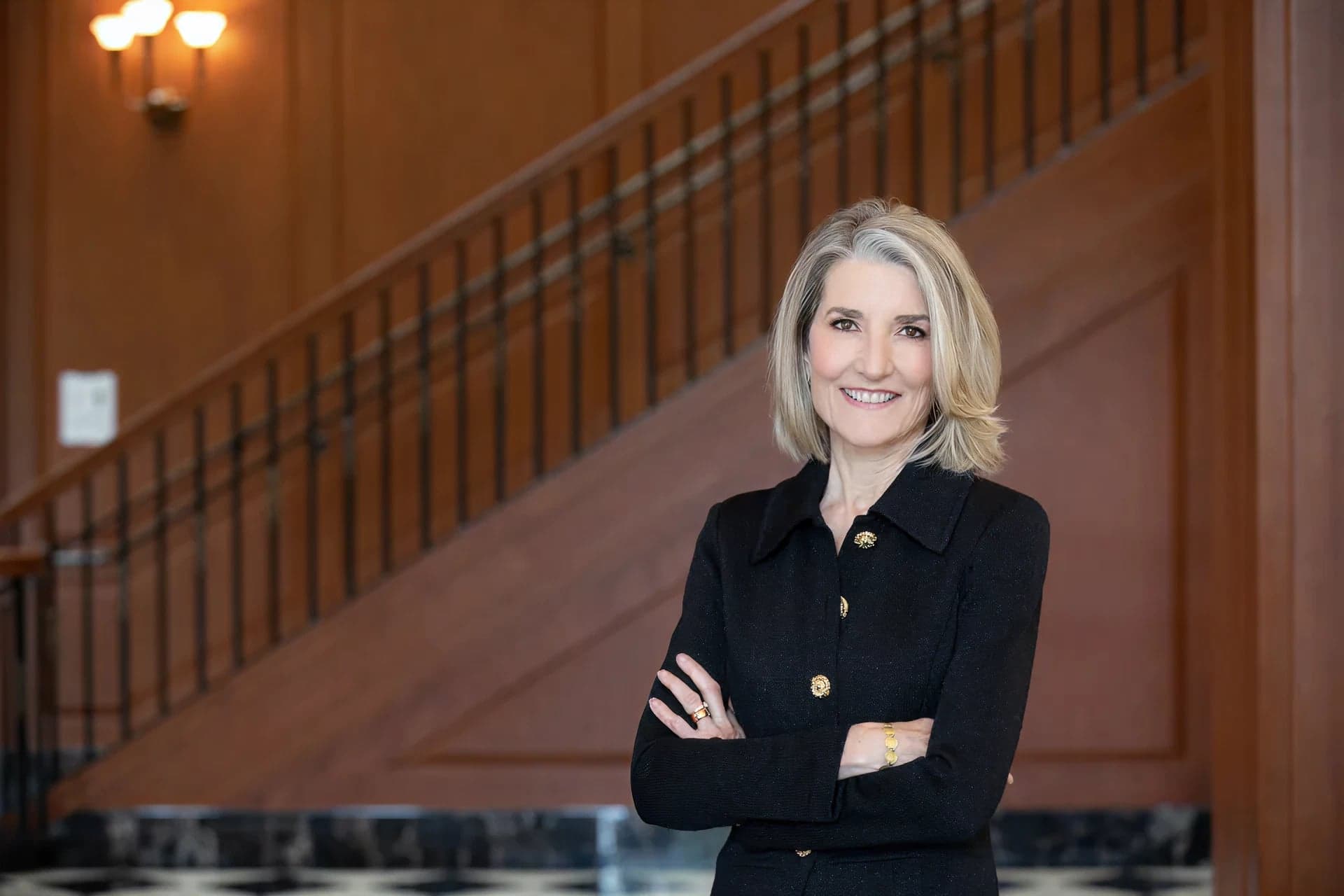 Amy Edmondson, Harvard Business School — arms folded, in a dark jacket, in front of a timber-and-brass staircase