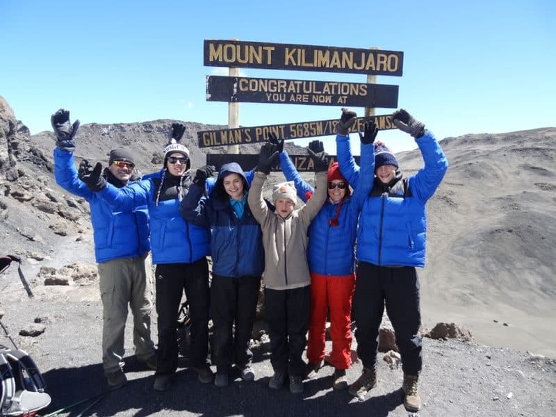 Margie Warrell and her climbing party at the Kilimanjaro summit sign, arms raised in celebration