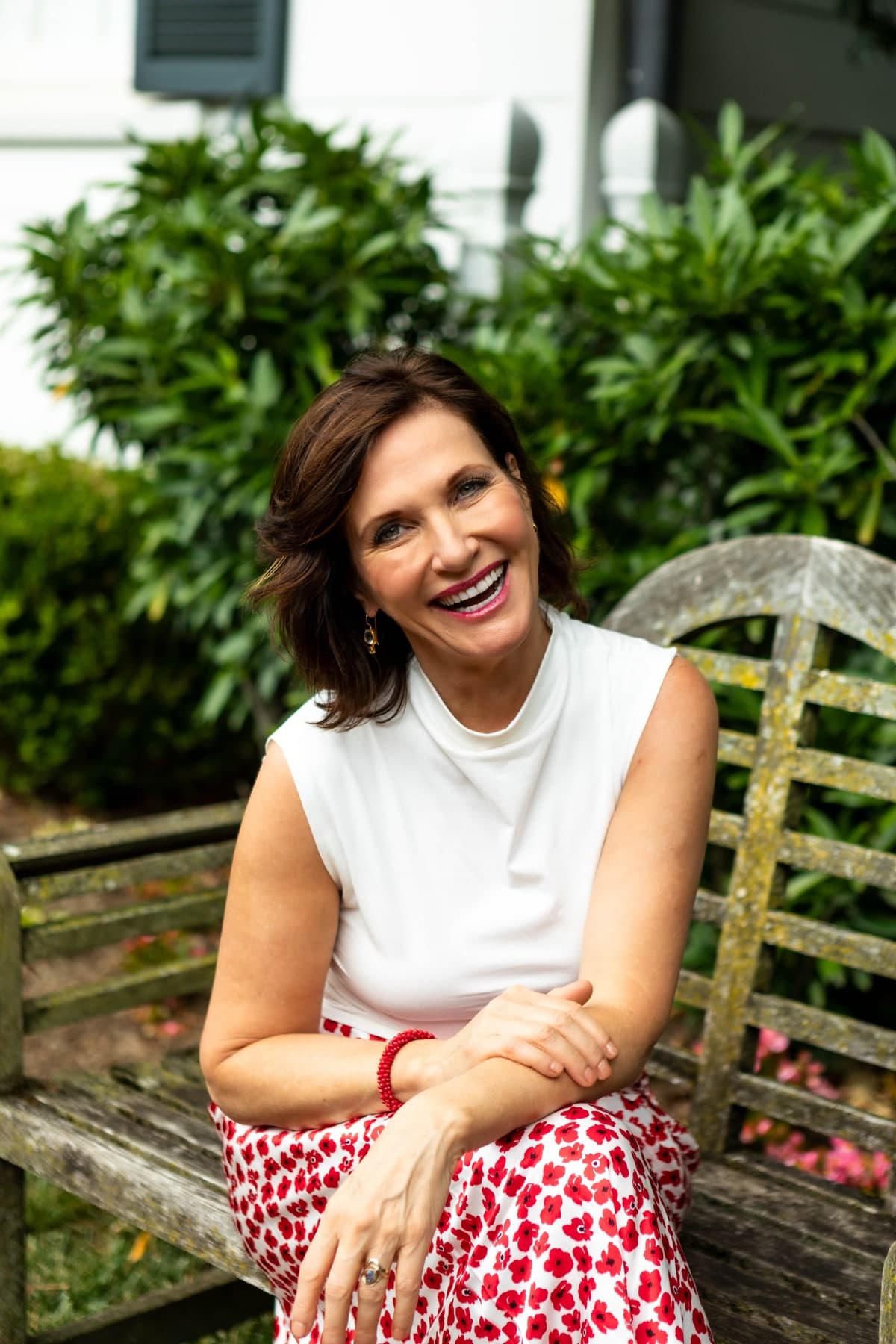 Margie Warrell laughing, seated on a weathered timber garden bench