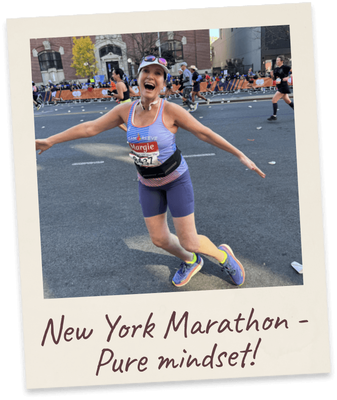 New York Marathon - Pure mindset! Margie mid-stride on a city marathon course, arms flung wide, race bib and visor.