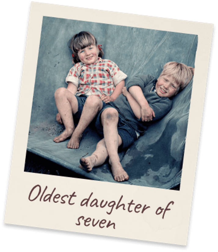 Oldest daughter of seven. Two barefoot children sitting side by side on a blue-grey timber deck.