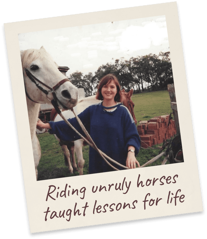 Riding unruly horses taught lessons for life. Margie as a young woman in a navy jumper holding the reins of a white horse in a paddock.