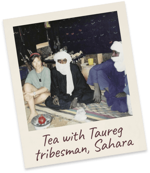 Tea with Taureg tribesman, Sahara. Margie seated cross-legged on a rug beside two robed Tuareg men with a tea tray, inside a tent.